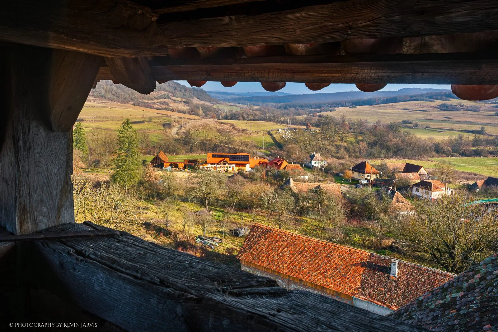 Șomartin from the church tower: the farm's orange roof among bare orchards, the hills beyond.