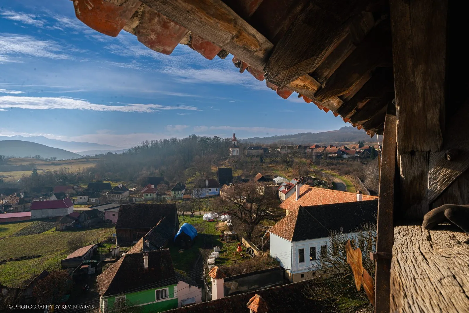 Under the tower's eaves: the village, the white church across the valley, mist on the hills.