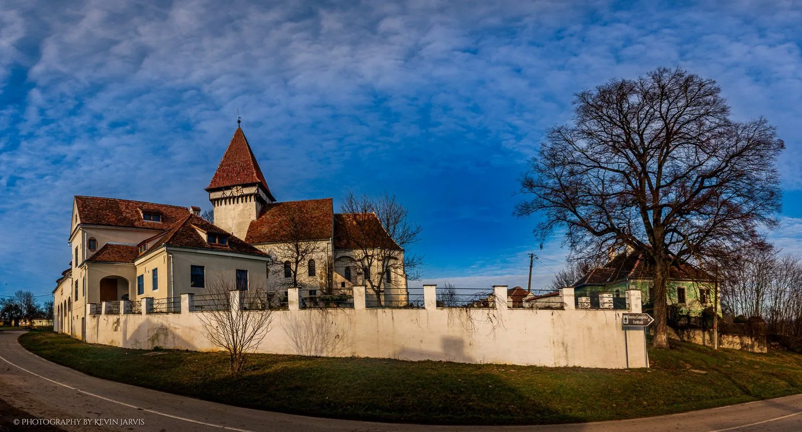The fortified church of Șomartin behind its white wall, the tower and the old lime tree against a winter sky.